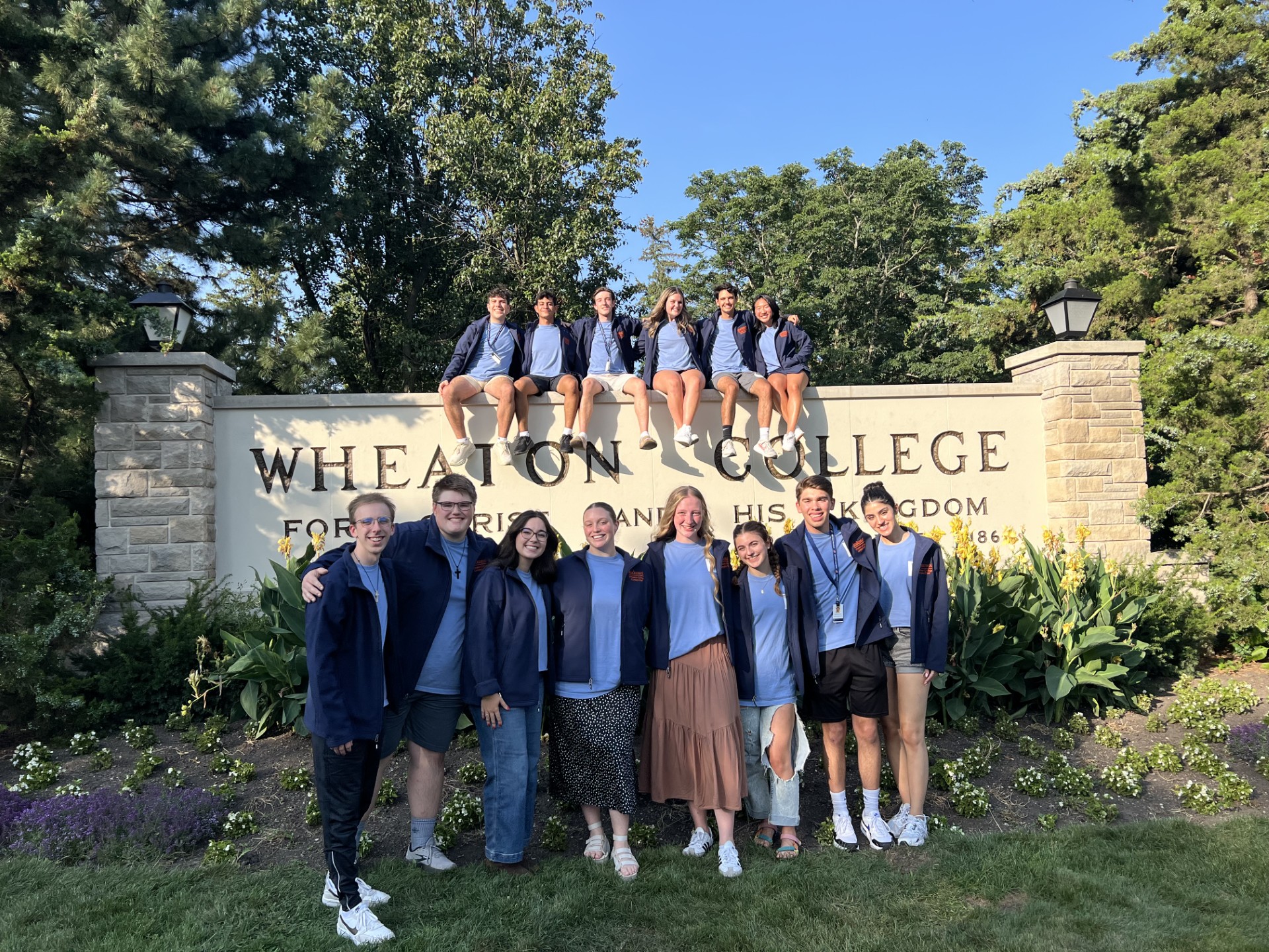 Group of students sitting and standing around Wheaton College sign