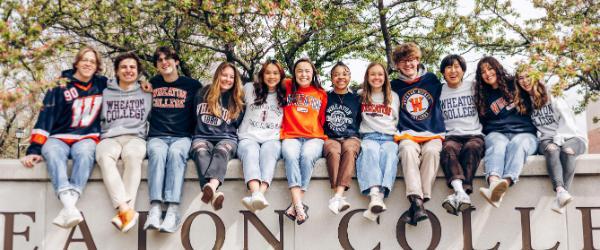 Wheaton IL Students sitting on Wheaton sign