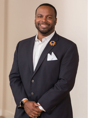 A black man wearing a suit and dress shirt smiles