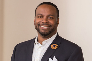 A black man wearing a suit and dress shirt smiles