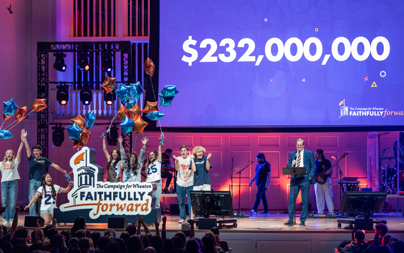 Numerous people stand on a stage holding a sign that reads Faithfully Forward while the screen behind them reads two hundred and thirty two million dollars